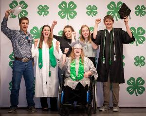 group with caps and gowns in front of clover backdrop